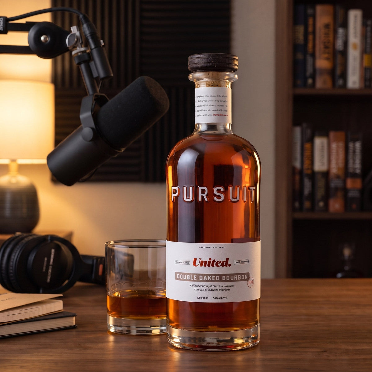 Pursuit United Double Oaked Bourbon, 108 proof, on a walnut desk in a home podcast studio beside a neat pour and a broadcast microphone