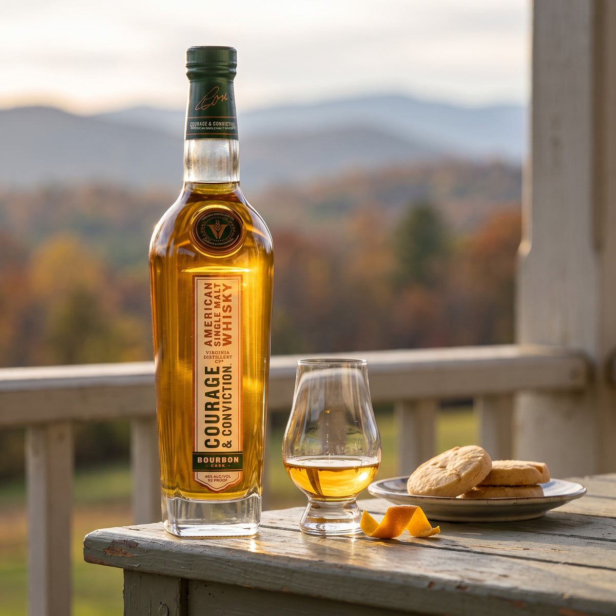 Courage &amp; Conviction Bourbon Cask American single malt on a porch rail with a Glencairn glass, shortbread and orange peel, Blue Ridge foothills in autumn