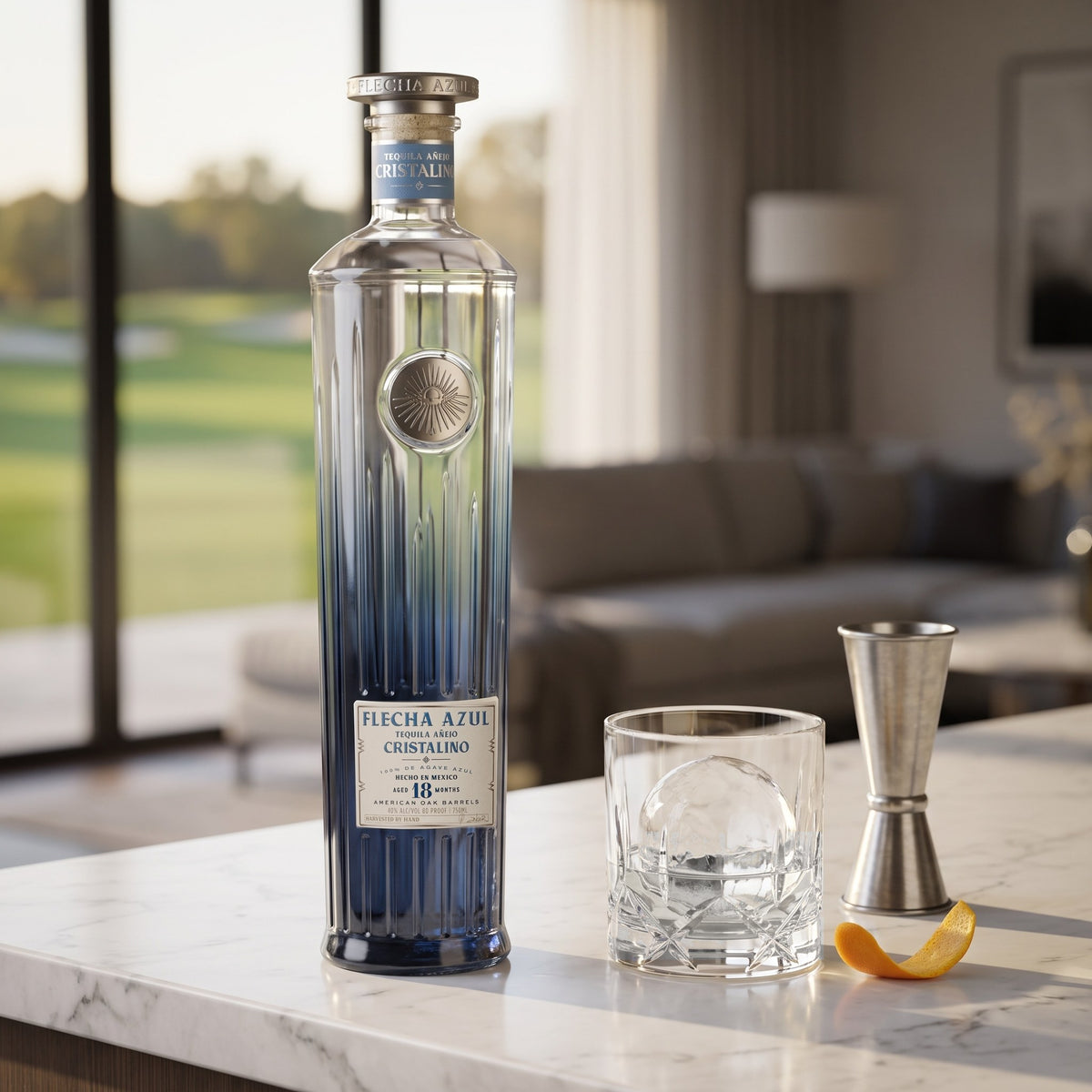 Flecha Azul Añejo Cristalino Tequila, 80 proof, on a white marble home bar beside a rocks glass with a clear ice sphere and an orange twist