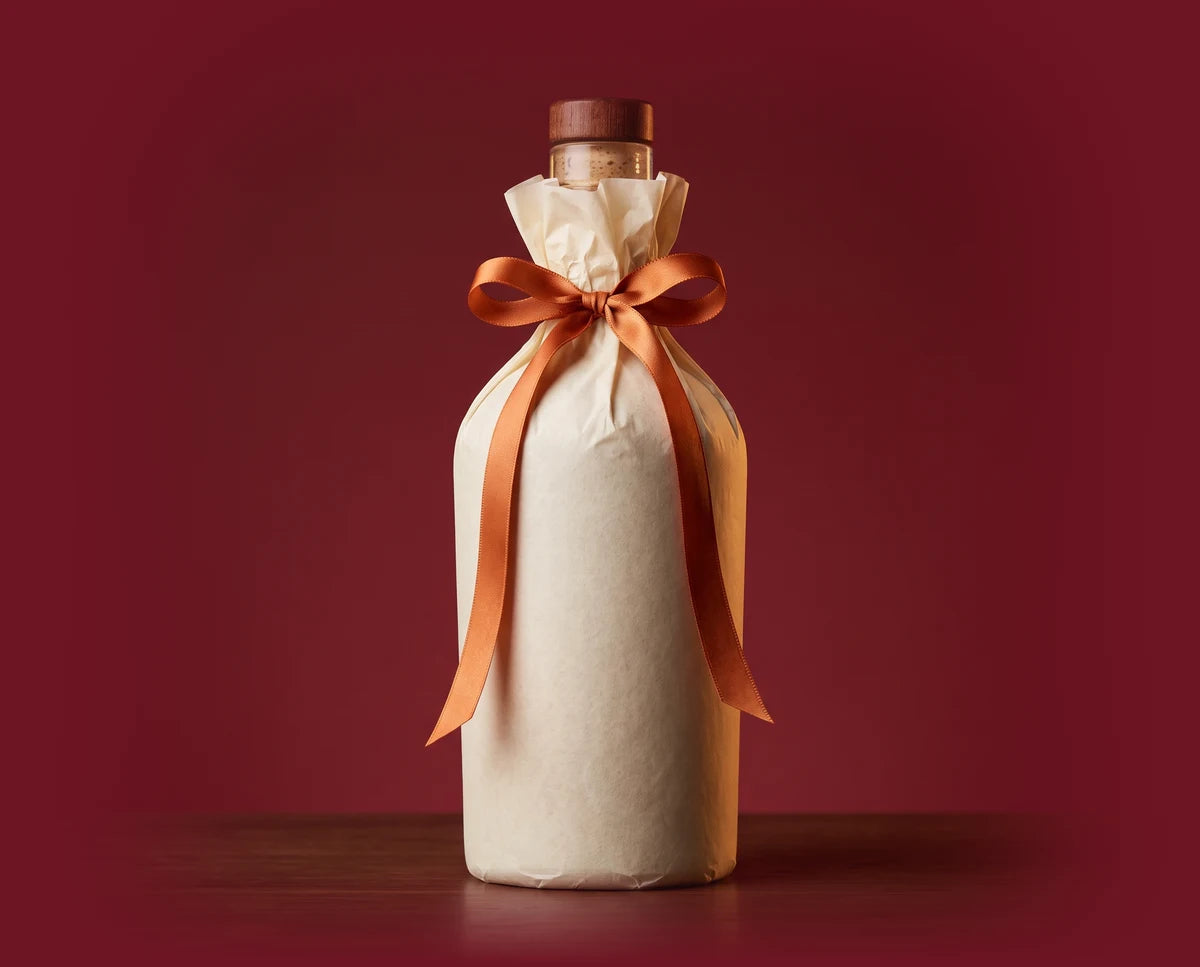 A whiskey bottle gift-wrapped in cream paper and tied with a copper satin bow